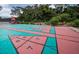 Colorful shuffleboard court with shaded seating, table, and surrounding landscaping and manicured hedges at 36750 Us Highway 19 N # 6-214, Palm Harbor, FL 34684