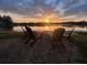 A serene outdoor space with Adirondack chairs surrounding a fire pit, set against a picturesque sunset over the lake at 1301 Jen Ma Jo Ln, Lutz, FL 33549