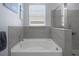 A white soaking tub is set below a window and against a backdrop of gray tiled walls at 13359 Golden Lime Ave, Spring Hill, FL 34609