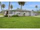 A gray single-story home surrounded by a lush green lawn and accented with vibrant tropical landscaping at 112 Rose St, Venice, FL 34293
