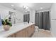 Bright bathroom with a wooden vanity, decorative plant, and a shower with gray curtain at 125 Island Way # 402, Clearwater Beach, FL 33767