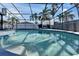 Sparkling swimming pool with screen enclosure, outdoor grill, and view of palm trees against blue sky at 1425 Monte Lake Dr, Valrico, FL 33596