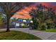 Charming blue two-story home with a long driveway and lush landscaping and mature trees at sunset at 1975 Levine Ln, Clearwater, FL 33760