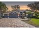 Charming single-story home featuring a three-car garage, brick driveway, and landscaped front yard at sunset at 10129 Paddock Oaks Dr, Riverview, FL 33569