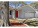 Home featuring a red front door, lush landscaping, and a well-maintained two car garage at 1582 Sandalwood Dr, Dunedin, FL 34698