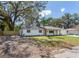 Exterior shot of a one-story white home with mature trees and a well-maintained lawn at 303 Suzette Dr, Brandon, FL 33511