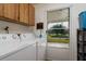 Well-lit laundry room with washer, dryer, wood cabinets, and screened exterior door at 9170 Dupont Ave, Spring Hill, FL 34608