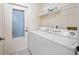 Well-lit laundry room featuring white washer and dryer, overhead shelving, and convenient access to the outside at 1022 Mctavish Way, Palm Harbor, FL 34684