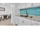 Bright kitchen with stainless steel sink, teal backsplash, white cabinets, and laminate countertops at 9715 Harrell Ave # 22, Treasure Island, FL 33706
