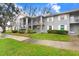A multi-unit gray apartment building has well-maintained lawns and is surrounded by trees at 1420 Oak Hill Dr # 102, Dunedin, FL 34698