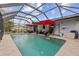 In-ground pool with screened enclosure, stone patio, and red umbrellas at 20191 Rutherford Ave, Port Charlotte, FL 33952