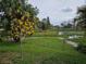 Scenic backyard view of a pond with lush greenery and a vibrant yellow blooming tree at 7730 Arlight Dr, New Port Richey, FL 34655