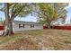Cozy single-story home with a neutral exterior, dark shutters, and surrounded by mature trees and a red fence at 7480 Hobson Ne St, St Petersburg, FL 33702