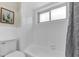 White bathroom with a window over tub, toilet, and gray shower curtain at 1510 Lakeside Dr, Dunedin, FL 34698