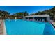 Community pool with lounge chairs and tables surrounded by mature landscaping under clear blue skies at 1182 Pine Ridge W Cir # B1, Tarpon Springs, FL 34688