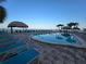 Lounge by the sparkling pool with a tiki hut and swaying palm trees, near the beach at 12924 Gulf Blvd # 110, St Petersburg, FL 33708