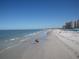 Beautiful sandy beach with condo buildings in the distance, with people walking on the shore at 450 S Gulfview Blvd # 605, Clearwater Beach, FL 33767