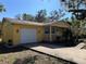 A cozy yellow home with a porch, attached garage, and mature landscaping in a sunny setting at 7111 N 53Rd St, Tampa, FL 33617