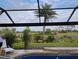A large yard with manicured tropical landscaping is visible from the enclosed pool at 28 Sportsman Pl, Rotonda West, FL 33947