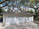 Three-car garage with white doors and detailed windows under mature trees at 13607 Mcintosh Rd, Thonotosassa, FL 33592