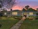 Charming stone home with mature landscaping, sidewalk and a well-manicured green lawn at dusk at 524 Park S St, St Petersburg, FL 33707