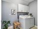 Well-lit laundry room with gray walls, white cabinets, washer, dryer, and a decorative plant at 8887 Little Bluestem Dr, Land O Lakes, FL 34637