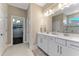 Bathroom with double sinks, white cabinetry, a shower with decorative tile, and access to the closet at 7096 Heron Walk Ln, Wesley Chapel, FL 33545