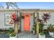 Inviting front porch with a bright coral door, stone walkway, and lush tropical plants at 6202 Tennessee Ave, New Port Richey, FL 34653