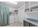 Functional laundry room with washer, dryer, storage shelves, and an ironing board for convenience at 6339 S Lansdale Cir, Tampa, FL 33616