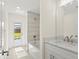 Bright bathroom features a tub with light tile surround, white cabinets with a marble countertop, and a window view to the yard at 7235 Peacock Ln, Englewood, FL 34224