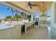 Outdoor kitchen featuring a grill, marble counters, sink, and ceiling fan for comfortable outdoor cooking and dining at 15904 Redington Dr, Redington Beach, FL 33708