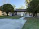 Charming single-story home with a concrete driveway framed by mature trees, a lawn, and an inviting front porch at 9873 88Th St, Seminole, FL 33777