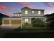 Charming two-story home with a well-manicured lawn, attached garage, and inviting curb appeal at dusk at 7811 Roma Dune Dr, Wesley Chapel, FL 33545
