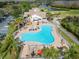 Aerial view of a kidney-shaped pool with lounge chairs, umbrellas, and palm trees, next to the clubhouse and golf course at 8141 Ambersweet Pl, Land O Lakes, FL 34637
