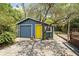 Backyard outbuilding with a garage door and yellow door, surrounded by trees and shrubbery at 5915 N Otis Ave, Tampa, FL 33604