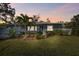 Charming home featuring a well-manicured lawn, lush landscaping, and mature palm trees, beautifully lit at dusk at 1269 80Th N Ave, St Petersburg, FL 33702