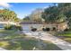 Single-story home with a long driveway, garage, mature trees, and a well-manicured front lawn at 1549 San Christopher Dr, Dunedin, FL 34698