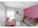 Charming Bedroom featuring a pink accent wall, a crib, a soft armchair, and a cozy ottoman at 15613 Charr Island St, Sun City Center, FL 33573