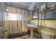 Bathroom with yellow-tiled walls, pedestal sink, and glass shelving unit, featuring a shower with curtain at 2501 Auburn S St, St Petersburg, FL 33712