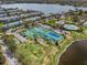 Aerial view showcasing tennis courts with lush landscaping, community buildings, and a tranquil lake at 4966 Coquina Key Se Dr # 4966, St Petersburg, FL 33705