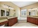 Bathroom with granite countertop dual sinks, ornate mirrors, and soaking tub under window at 15908 Cobble Mill Dr, Wimauma, FL 33598