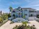 Stunning three-story blue home featuring a grand staircase, multiple balconies, lush landscaping, and brick driveway at 289 8Th N Ave, Tierra Verde, FL 33715