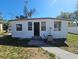 Modest single-story home with white siding, multiple windows, and a concrete walkway leading to the entrance at 4501 67Th N St, St Petersburg, FL 33709