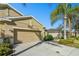 Exterior view of a tan home with a two car garage and lush tropical landscaping on a bright sunny day at 2253 Oakley Green Dr # 26, Sun City Center, FL 33573
