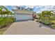 Charming front exterior view featuring a two-car garage, lush landscaping, and a brick paver driveway at 5232 Wishing Arch Dr, Apollo Beach, FL 33572