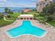 Aerial view of a uniquely shaped pool with lounge chairs, a cabana, and the waterfront in the background at 634 Edgewater Dr # 744, Dunedin, FL 34698