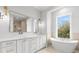 Bathroom with double sink vanity with white cabinets, gold hardware, and soaking tub near a window at 216 N Hesperides St, Tampa, FL 33609