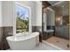 Bright bathroom featuring a soaking tub by a window and glass enclosed shower with brown tile and gold hardware at 216 N Hesperides St, Tampa, FL 33609