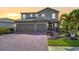 Two-story home featuring a two-car garage, brick driveway, manicured landscaping, and a palm tree in the front yard at 11605 Cleyera Ct, Riverview, FL 33579