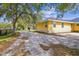 Side view of a charming yellow home with mature trees, gravel drive, and a glimpse of a barn at 12840 State Road 62, Parrish, FL 34219